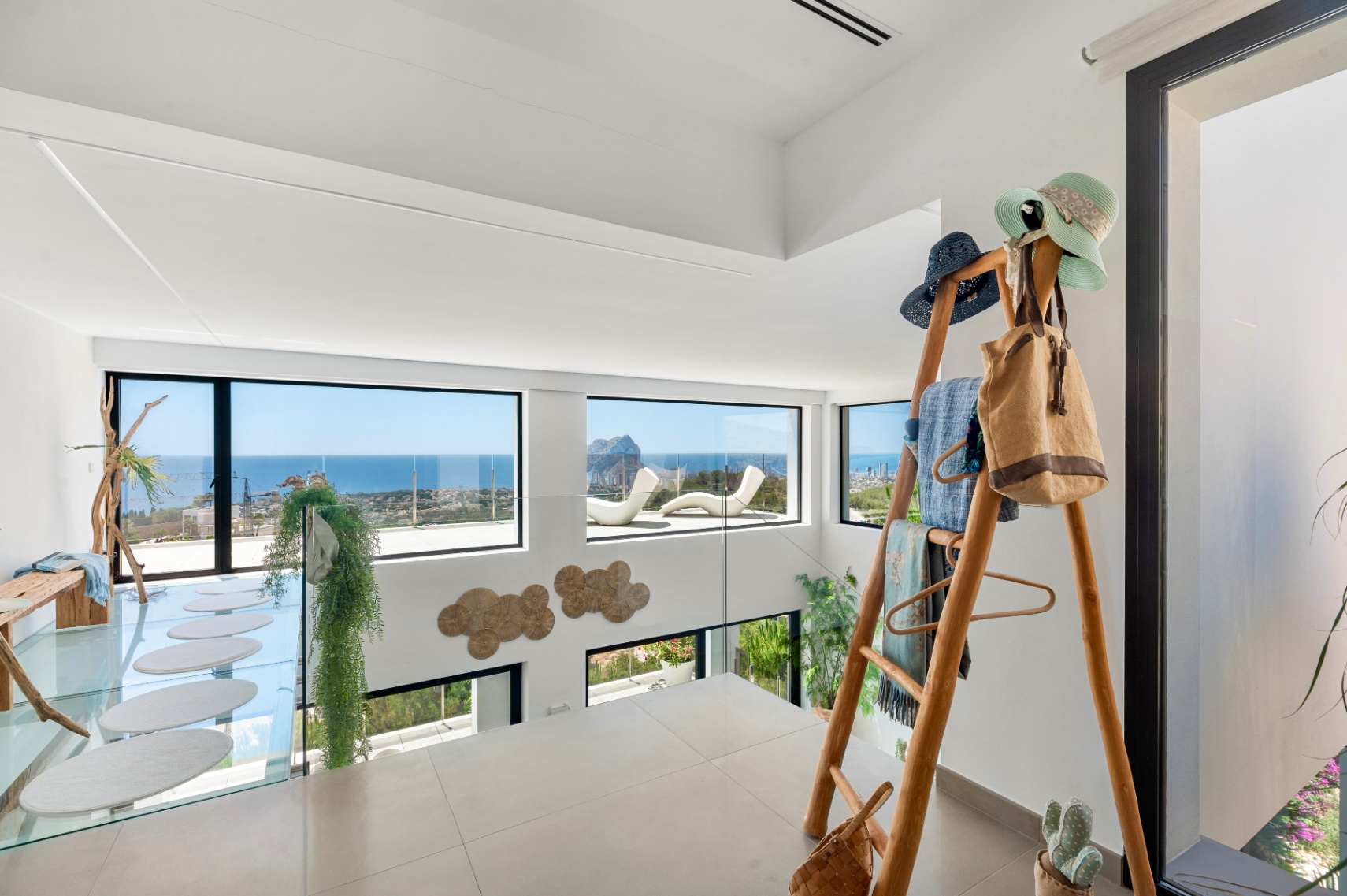 Bovenverdieping met lichte tegels en glazen balustrade. Grote ramen bieden panoramisch uitzicht op zee en de Peñon de Ifach. Kenmerken omvatten een glazen loopbrug met ovale treden en een houten rek. Bovenverdieping met lichte tegels en glazen balustrade. Grote ramen bieden panoramisch uitzicht op zee en de Peñon de Ifach. Kenmerken omvatten een glazen loopbrug met ovale treden en een houten rek.