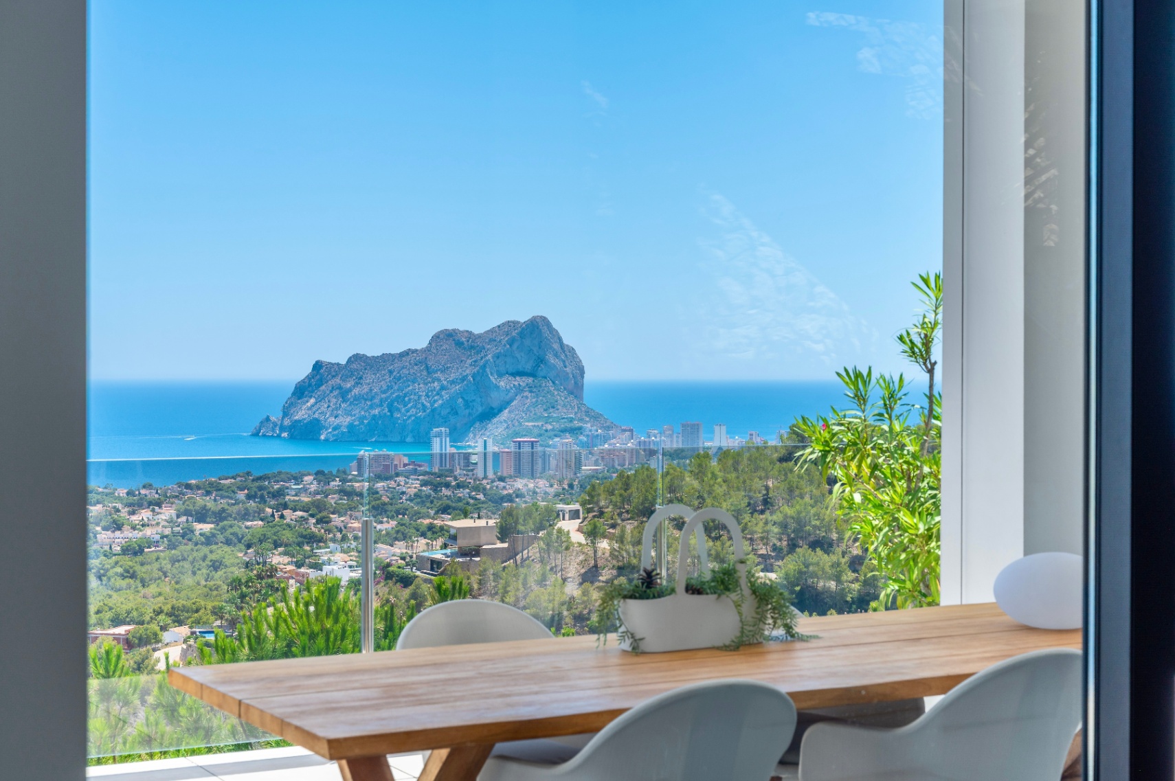 Buiten eetgedeelte met een houten tafel en moderne witte stoelen, met panoramisch uitzicht op de Peñon de Ifach, de Middellandse Zee en de kustlijn van Calpe. Buiten eetgedeelte met een houten tafel en moderne witte stoelen, met panoramisch uitzicht op de Peñon de Ifach, de Middellandse Zee en de kustlijn van Calpe.