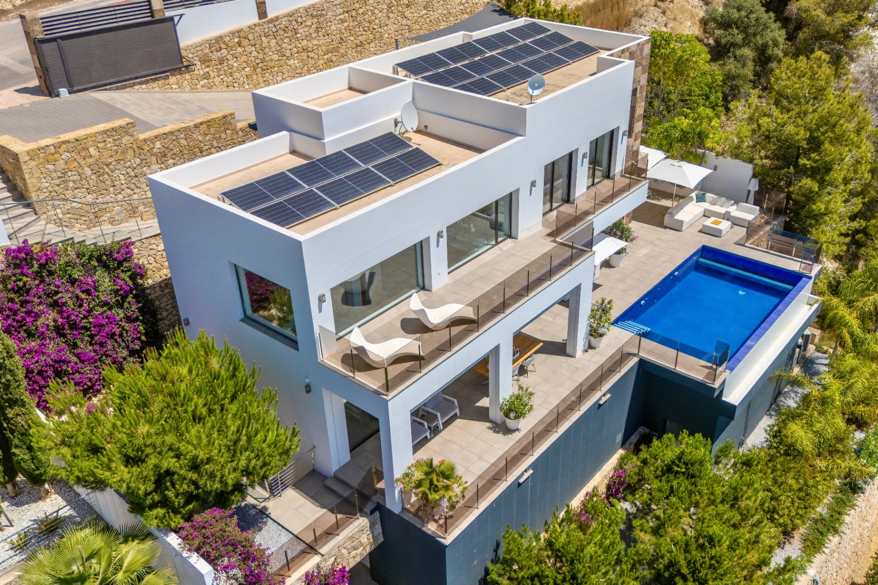 Luchtfoto van een moderne witte villa met meerdere terrasniveaus, een rechthoekig zwembad en ruime buitenlounges. Zonnepanelen zijn zichtbaar op de platte daken, omringd door weelderige mediterrane beplanting. Luchtfoto van een moderne witte villa met meerdere terrasniveaus, een rechthoekig zwembad en ruime buitenlounges. Zonnepanelen zijn zichtbaar op de platte daken, omringd door weelderige mediterrane beplanting.