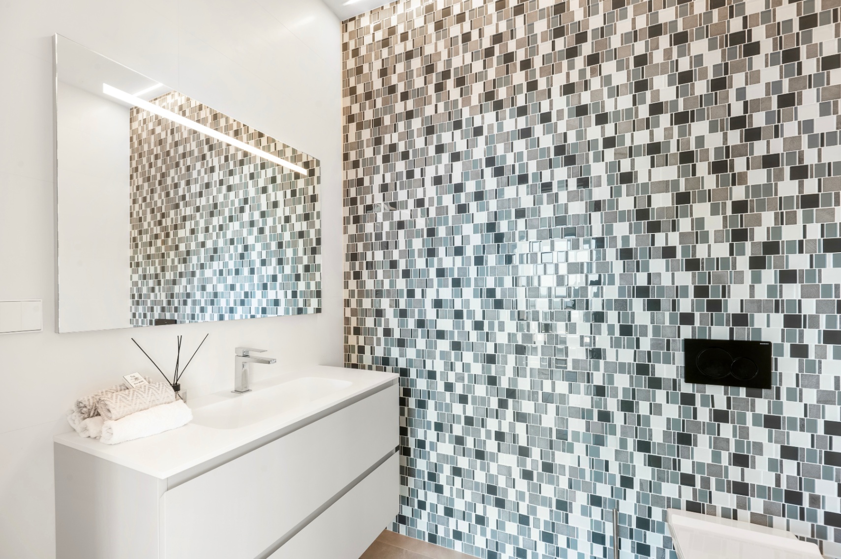 Moderne badkamer met een wit zwevend badmeubel en geïntegreerde wastafel. De accentmuur is bekleed met grijs-witte mozaïektegels, gecombineerd met een verlichte spiegel. Moderne badkamer met een wit zwevend badmeubel en geïntegreerde wastafel. De accentmuur is bekleed met grijs-witte mozaïektegels, gecombineerd met een verlichte spiegel.