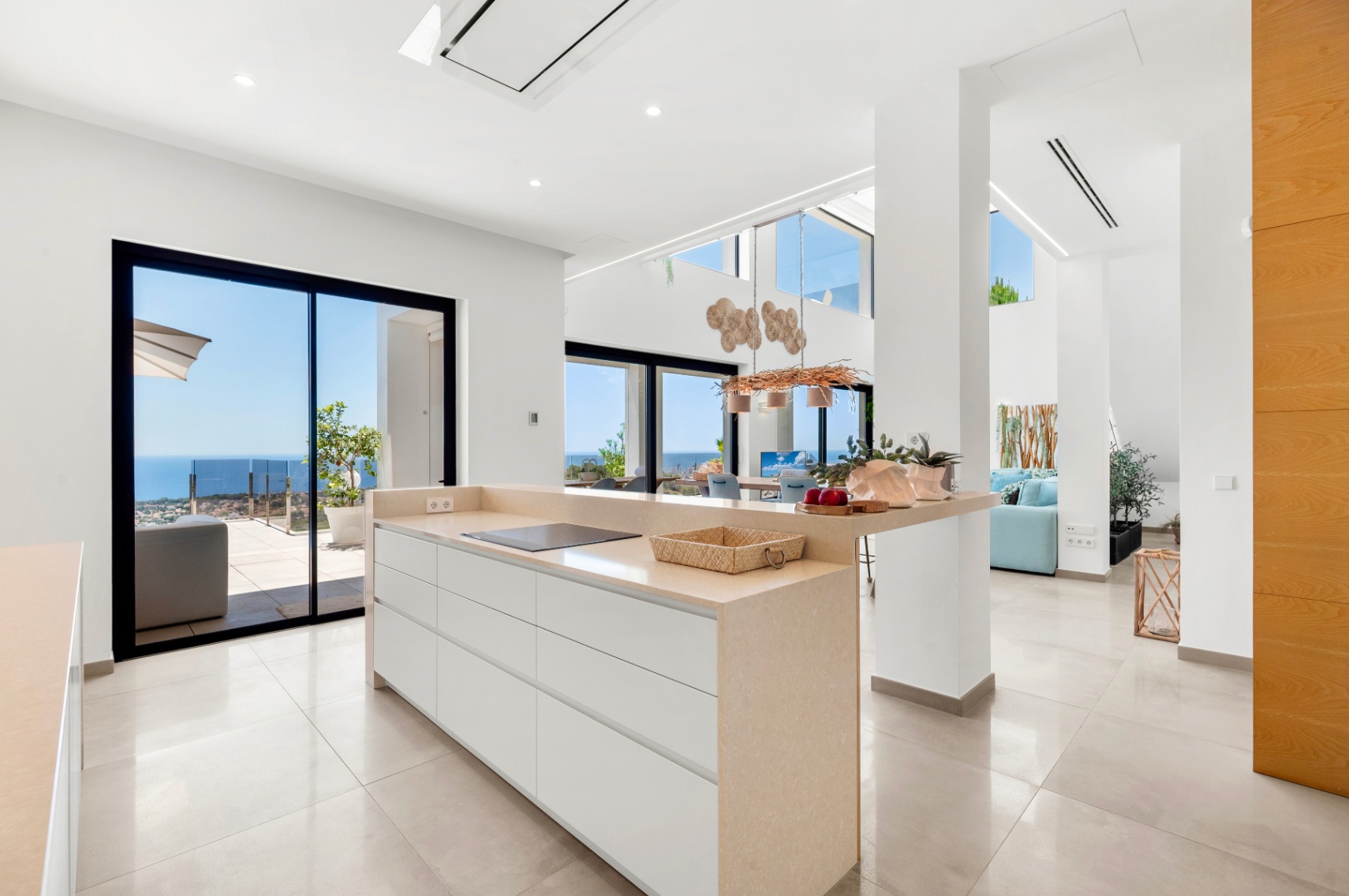 Moderne open keuken met centraal eiland, beige aanrechtblad en geïntegreerde inductiekookplaat. Grote glazen schuifdeuren bieden direct uitzicht op de Middellandse Zee, wat de lichte, eigentijdse ruimte versterkt. Moderne open keuken met centraal eiland, beige aanrechtblad en geïntegreerde inductiekookplaat. Grote glazen schuifdeuren bieden direct uitzicht op de Middellandse Zee, wat de lichte, eigentijdse ruimte versterkt.
