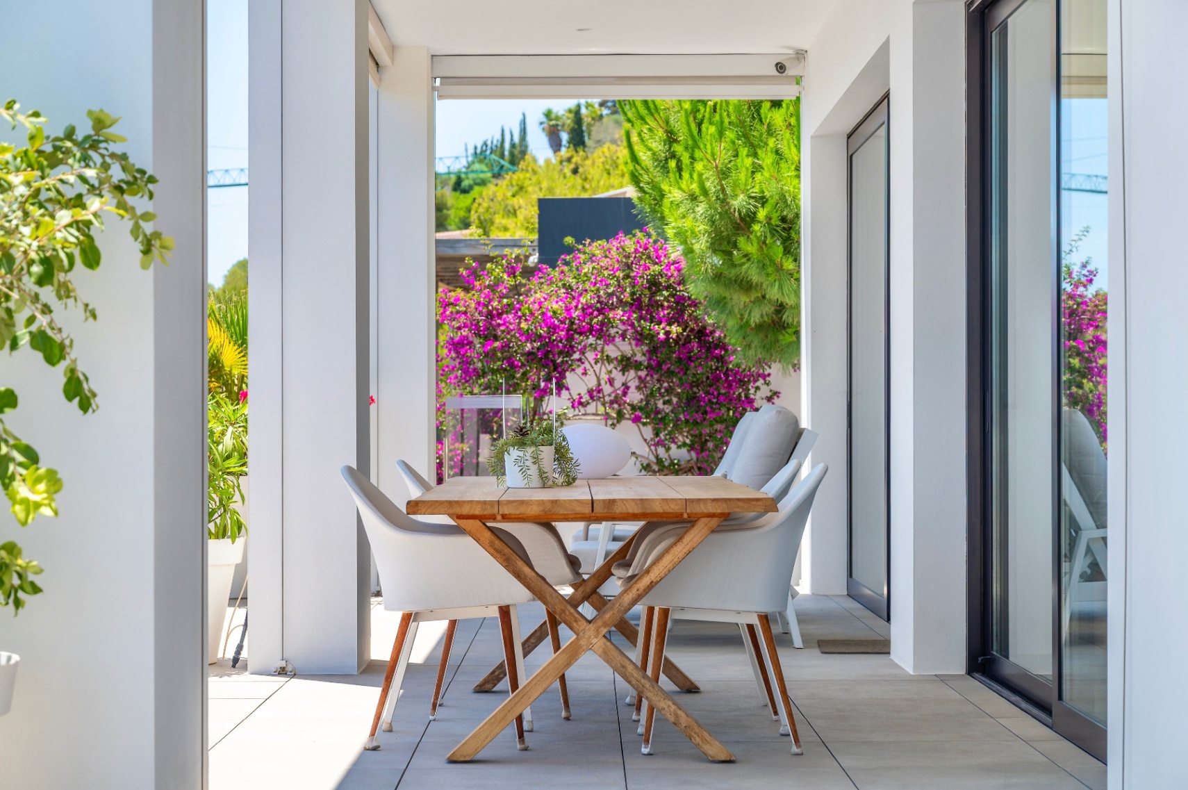 Overdekt buitenterras met een houten eettafel en witte stoelen, omlijst door weelderig groen en levendige bougainvillea, ideaal voor buitenmaaltijden. Overdekt buitenterras met een houten eettafel en witte stoelen, omlijst door weelderig groen en levendige bougainvillea, ideaal voor buitenmaaltijden.