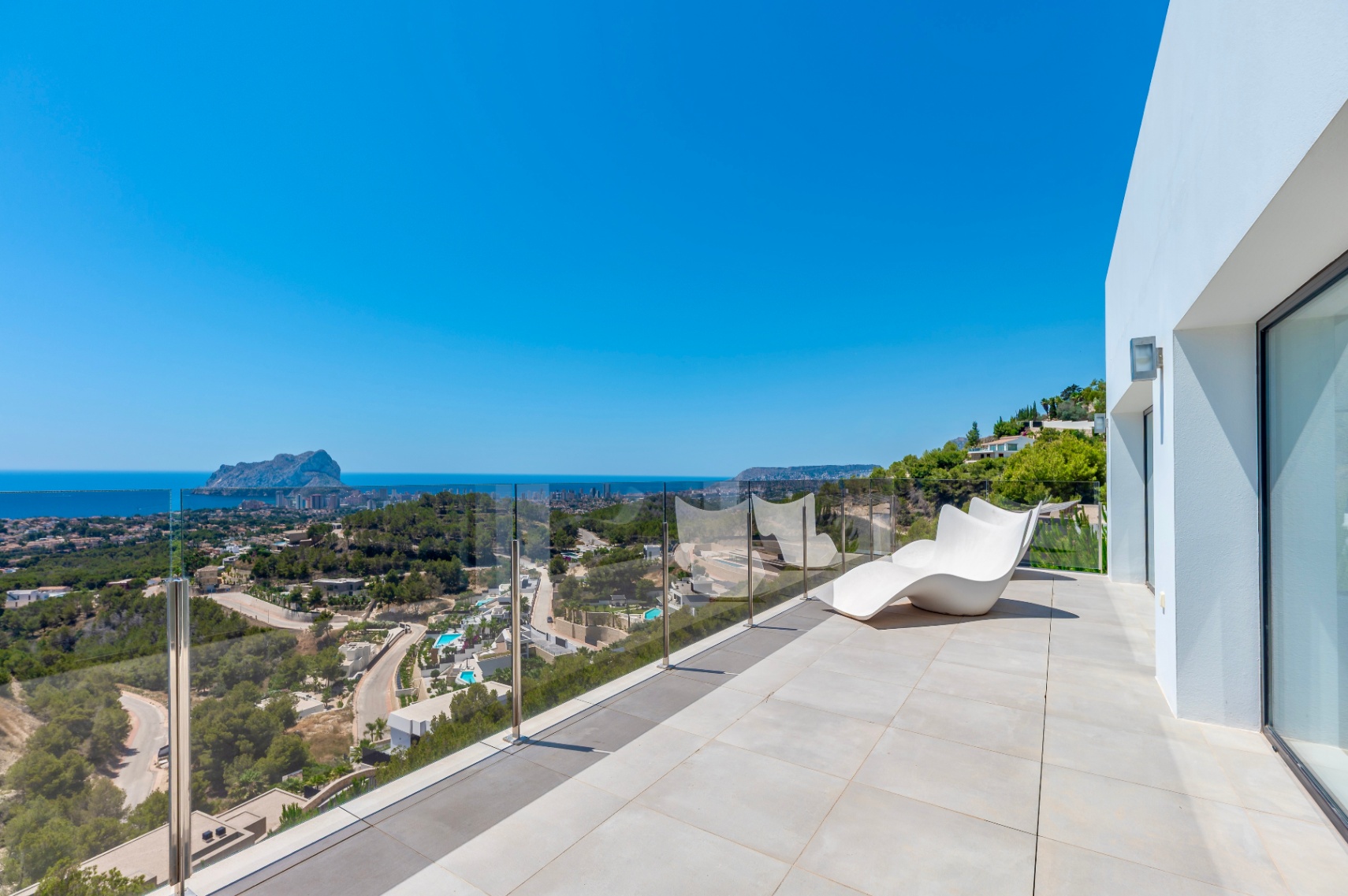 Ruim buitenterras met lichte tegels, een moderne witte ligstoel en een glazen balustrade. Geniet van panoramisch uitzicht op de Middellandse Zee, de Peñón de Ifach en de kust van Calpe. Ruim buitenterras met lichte tegels, een moderne witte ligstoel en een glazen balustrade. Geniet van panoramisch uitzicht op de Middellandse Zee, de Peñón de Ifach en de kust van Calpe.