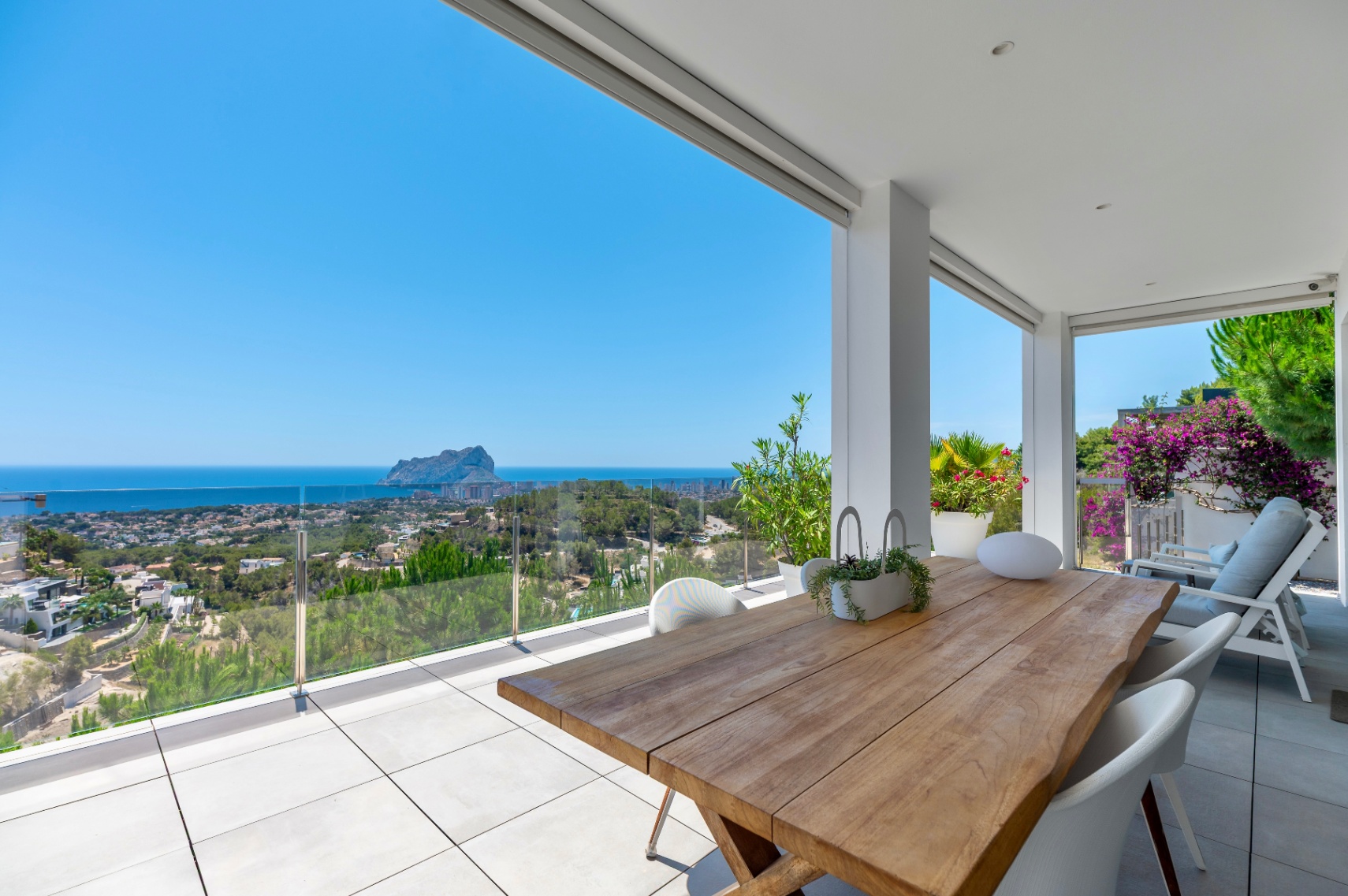 Ruime overdekte terras met een massief houten eettafel en witte stoelen. Biedt panoramisch uitzicht op de zee, Calpe en de Peñón de Ifach via een glazen balustrade. Ruime overdekte terras met een massief houten eettafel en witte stoelen. Biedt panoramisch uitzicht op de zee, Calpe en de Peñón de Ifach via een glazen balustrade.