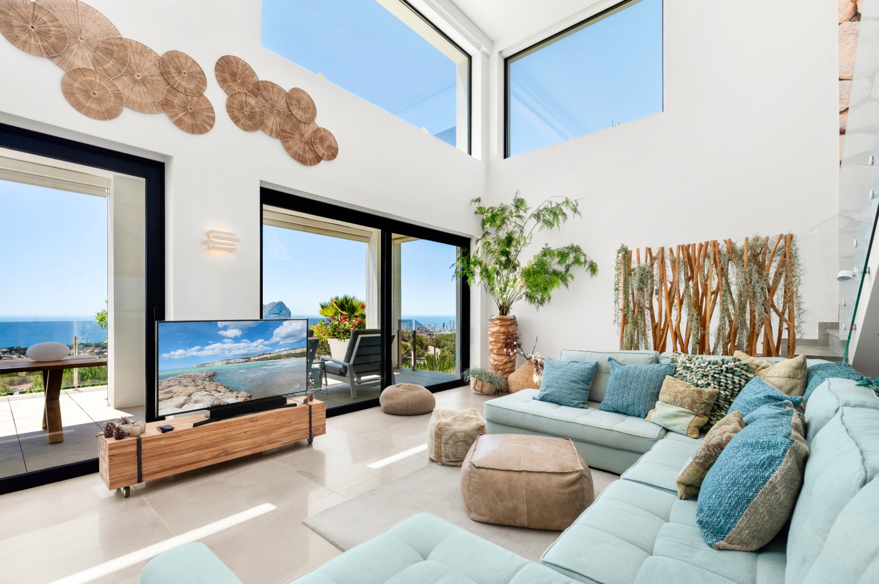Ruime woonkamer met hoge plafonds, grote glazen schuifdeuren en bovenramen die panoramisch zeezicht bieden. Een lichtblauwe hoekbank combineert met natuurlijke houten accenten en wanddecoratie. Ruime woonkamer met hoge plafonds, grote glazen schuifdeuren en bovenramen die panoramisch zeezicht bieden. Een lichtblauwe hoekbank combineert met natuurlijke houten accenten en wanddecoratie.