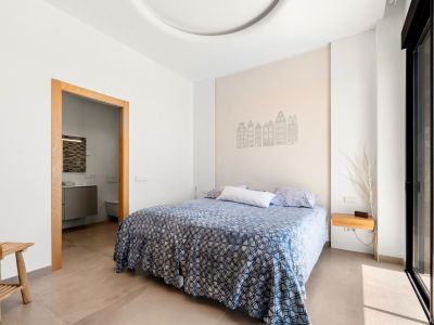 Lichte slaapkamer met tweepersoonsbed en een accentmuur met gebouwensilhouetten. Directe toegang tot een en-suite badkamer en een terras via een grote glazen schuifdeur.