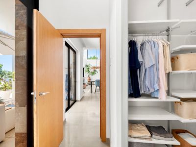 Moderne halingang met open lichte houten deur, die een ingebouwde witte kledingkast met verstelbare planken en een zonnig terras met zeezicht onthult.