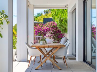 Overdekt buitenterras met een houten eettafel en witte stoelen, omlijst door weelderig groen en levendige bougainvillea, ideaal voor buitenmaaltijden.
