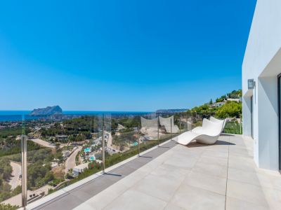 Ruim buitenterras met lichte tegels, een moderne witte ligstoel en een glazen balustrade. Geniet van panoramisch uitzicht op de Middellandse Zee, de Peñón de Ifach en de kust van Calpe.
