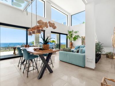 Ruime open woon- en eetkamer met hoge plafonds, grote ramen en een unieke takkenkroonluchter. Panoramisch uitzicht op zee, de kustlijn en de Peñón de Ifach kenmerken deze lichte ruimte.
