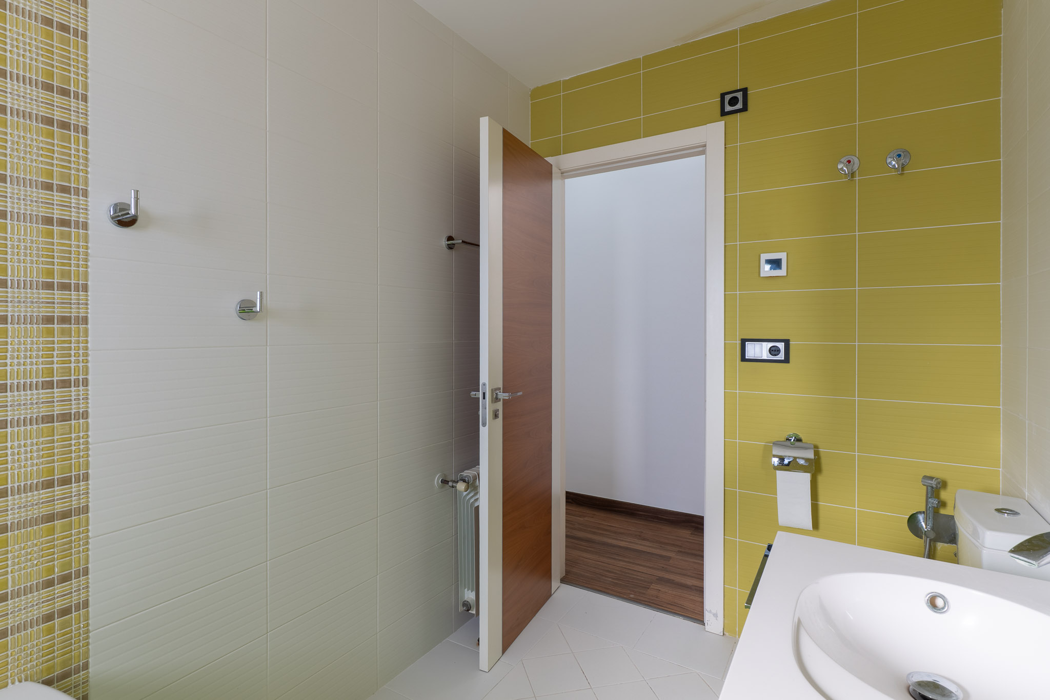 Moderne badkamer met levendige limoengroene en getextureerde beige wandtegels, verrijkt met een mozaïekaccent. Voorzien van een eigentijdse wastafel en een houten deur.