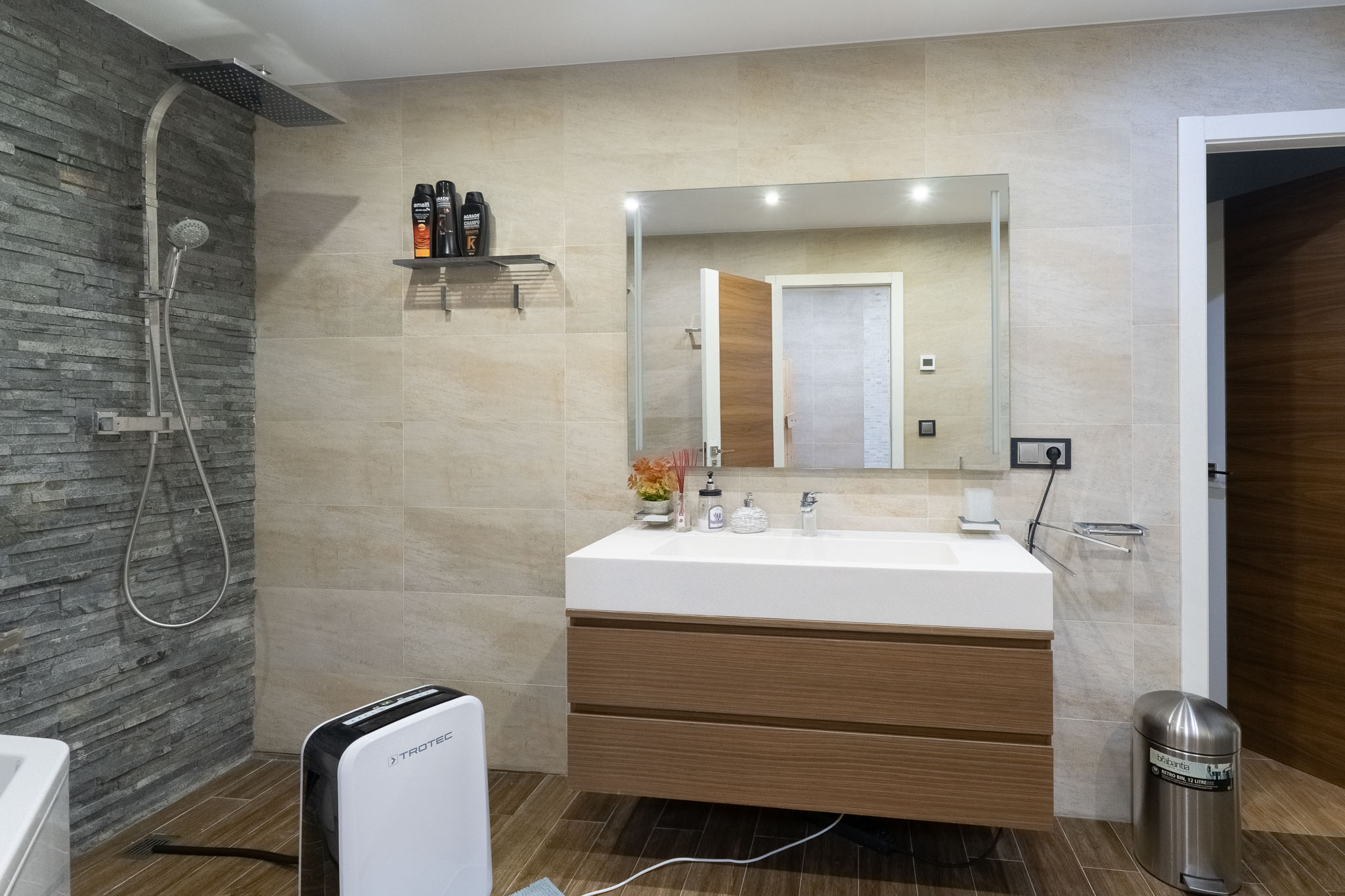 Moderne badkamer met regendouche en leisteen-accentmuur, zwevend houten wastafelmeubel en geïntegreerde wasbak. Tegels met houtlook op de vloer.