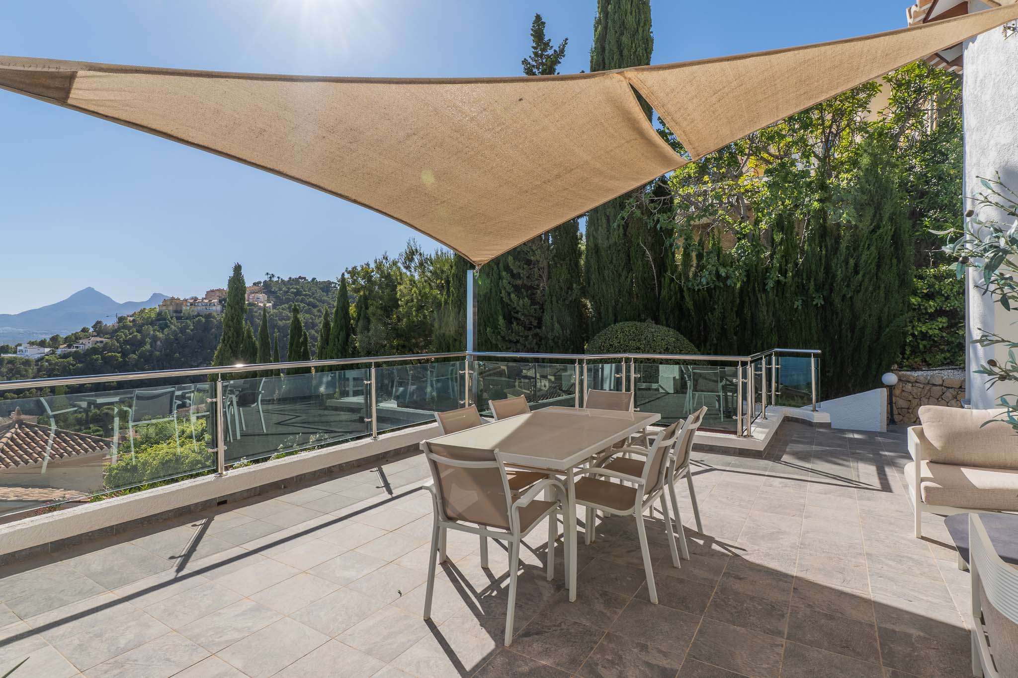 Ruim buitenterras met schaduwdoek, voorzien van eettafel en glazen balustrade, met panoramisch uitzicht op de bergen en de urbanisatie.