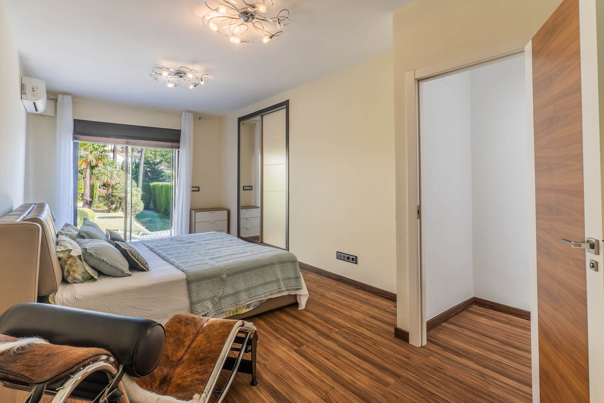 Slaapkamer met directe toegang tot de tuin via glazen schuifdeuren, laminaatvloer en spiegelende schuifdeurkast. Een open inloopkastruimte is zichtbaar.