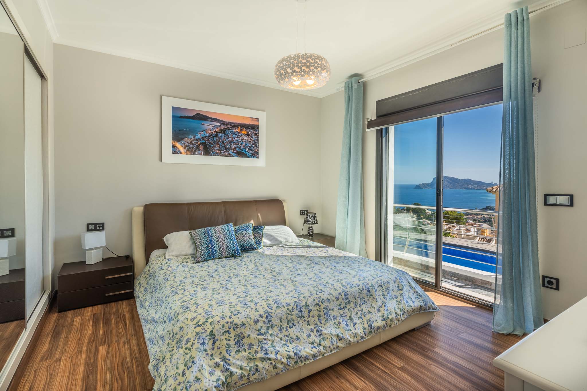 Slaapkamer met tweepersoonsbed, houten laminaatvloer en panoramisch uitzicht op zee via de grote schuifpui. Inclusief spiegelkast.