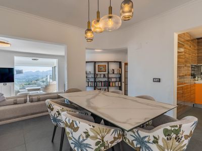 Design eetruimte met marmer-effect tafel en gestoffeerde stoelen, verlicht door moderne hanglampen. Grenst aan de woonkamer met panoramisch uitzicht op de bergen.