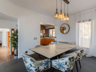 Eetruimte met marmerlook tafel en stoelen met tropisch patroon. Moderne hanglampen verlichten de ruimte, die open is naar een keuken met oranje kasten.