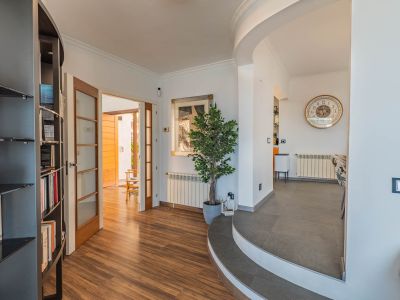 Entreehal met hout-look laminaatvloer, leidend naar buiten via glazen deuren. Gebogen tegelstappen verbinden met de eetruimte, gecompleteerd door een ingebouwde boekenkast.
