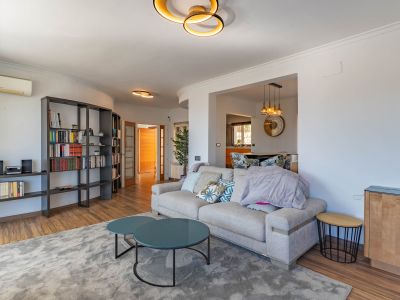 Hedendaagse woonkamer met lichte bank, twee ronde teal salontafels en een grote donkere modulaire boekenkast. Design plafondverlichting siert de ruimte.