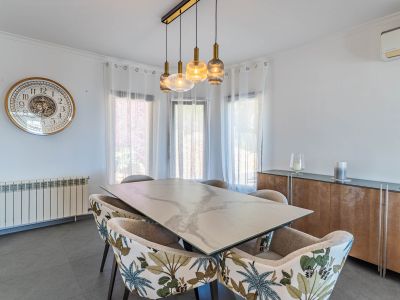 Lichte eetkamer met marmerlook tafel, stoelen met tropisch patroon en een moderne lineaire hanglamp, verlicht door natuurlijk licht.