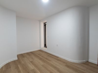 Lichte ruimte met lichte plankenvloer, witte muren en een opvallende gebogen wand. Voorzien van een smalle donker omlijste opening met stenen dorpel.
