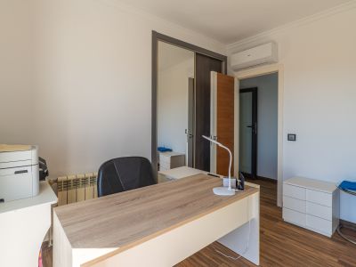Lichte studeerkamer met licht houten bureau, laminaatvloer, spiegelende schuifdeurkast en een airconditioningunit.