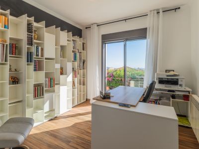 Lichte thuiskantoor met een wit modulair boekenkastsysteem, houten vloer en een modern bureau voor een balkon met weelderig groen uitzicht. Natuurlijk licht vult de ruimte.