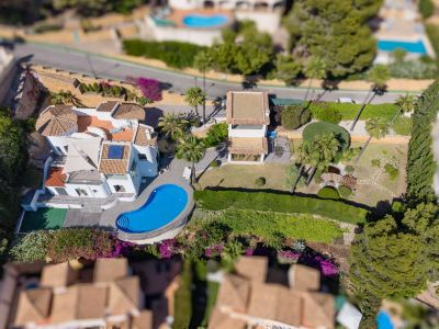 Luchtfoto van de villa met onregelmatig gevormd zwembad, uitgestrekte vlakke tuinen met vijver en een apart bijgebouw. Opvallend zijn de traditionele pannendaken en weelderige mediterrane beplanting.