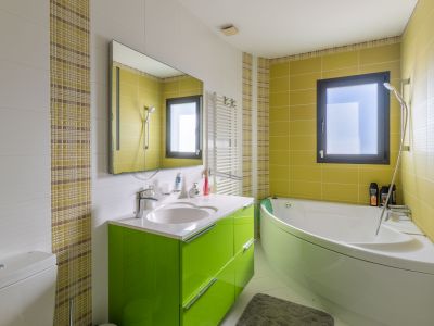 Moderne badkamer met hoekbad en een felgroen wastafelmeubel. Muren voorzien van witte structuur-, limoengroene en geruite mozaïektegels. Inclusief raam en handdoekradiator.