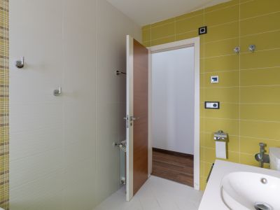 Moderne badkamer met levendige limoengroene en getextureerde beige wandtegels, verrijkt met een mozaïekaccent. Voorzien van een eigentijdse wastafel en een houten deur.