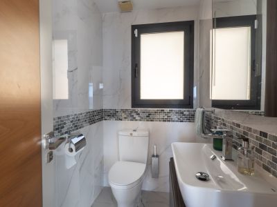 Moderne badkamer met witte marmerlook tegels, een grijze mozaïekrand en een donker kozijnraam. Voorzien van een strakke witte wastafel en bijpassend toilet.