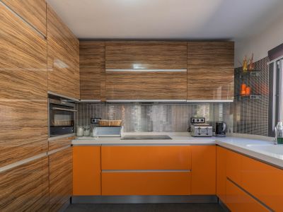 Moderne keuken met glanzende houtnerf bovenkasten en levendige oranje onderkasten, aangevuld met lichte werkbladen en een metallic mozaïek achterwand.