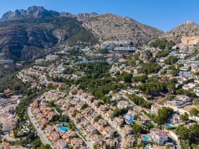 Panoramisch luchtbeeld van Altea Hills, met talloze villa's met zwembaden op de groene heuvel, tegen een indrukwekkend berglandschap.