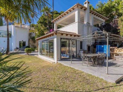 Ruim betegeld terras met eethoek onder een metalen pergola, grenzend aan een glazen serre en een verzorgde mediterrane tuin.