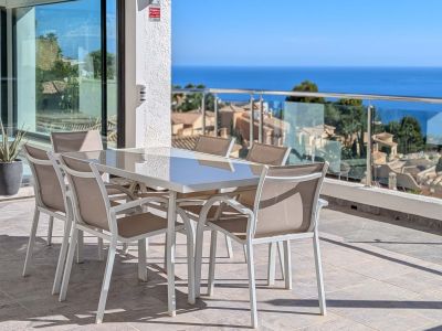 Ruim buitenterras met eettafel en stoelen, met panoramisch uitzicht op de Middellandse Zee en de daken van Altea Hills. Glazen schuifdeuren verbinden met het interieur.