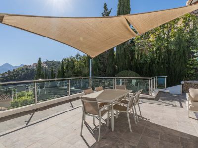 Ruim buitenterras met schaduwdoek, voorzien van eettafel en glazen balustrade, met panoramisch uitzicht op de bergen en de urbanisatie.