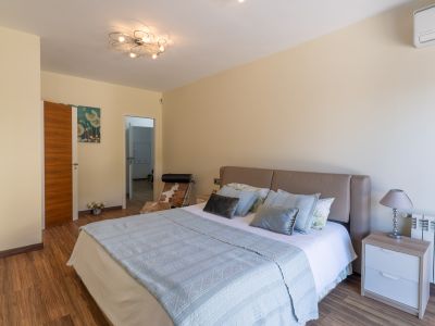 Slaapkamer met beige hoofdeinde, laminaatvloer en moderne plafondlamp. Een nachtkastje met lamp, radiator en airconditioning zijn zichtbaar.