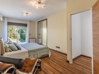 Slaapkamer met directe toegang tot de tuin via glazen schuifdeuren, laminaatvloer en spiegelende schuifdeurkast. Een open inloopkastruimte is zichtbaar.