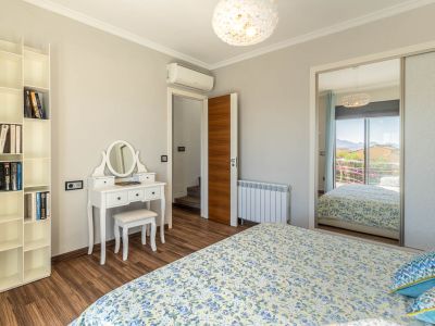 Slaapkamer met laminaatvloer, witte kaptafel en modulair boekenrek. De spiegelkast reflecteert een berguitzicht vanaf het balkon.