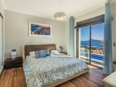 Slaapkamer met tweepersoonsbed, houten laminaatvloer en panoramisch uitzicht op zee via de grote schuifpui. Inclusief spiegelkast.