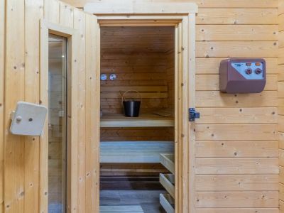 Toegang tot de sauna met lichte houten lambrisering, tonend de binnenbanken, een emmer met lepel en het externe bedieningspaneel.