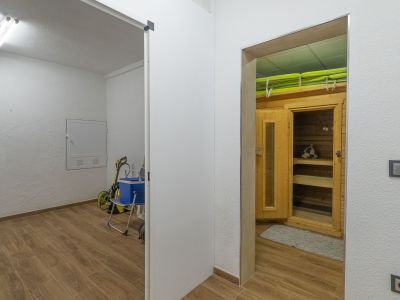 Toegewijde wellnessruimte met houten saunacabine en banken, grenzend aan een praktische bijkeuken. Beide ruimtes hebben een consistente houtnerf tegelvloer.