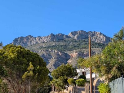 Uitzicht op de majestueuze Sierra de Bernia, met zijn rotsachtige toppen en groene hellingen, omlijst door de weelderige mediterrane vegetatie van het pand.