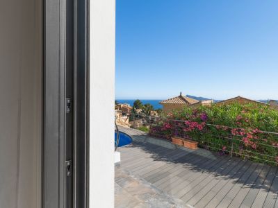 Zicht vanuit de schuifdeur op het terras met composiet vlonder, een glimp van het zwembad en stalen balustrade. De Middellandse Zee en traditionele daken zijn zichtbaar.