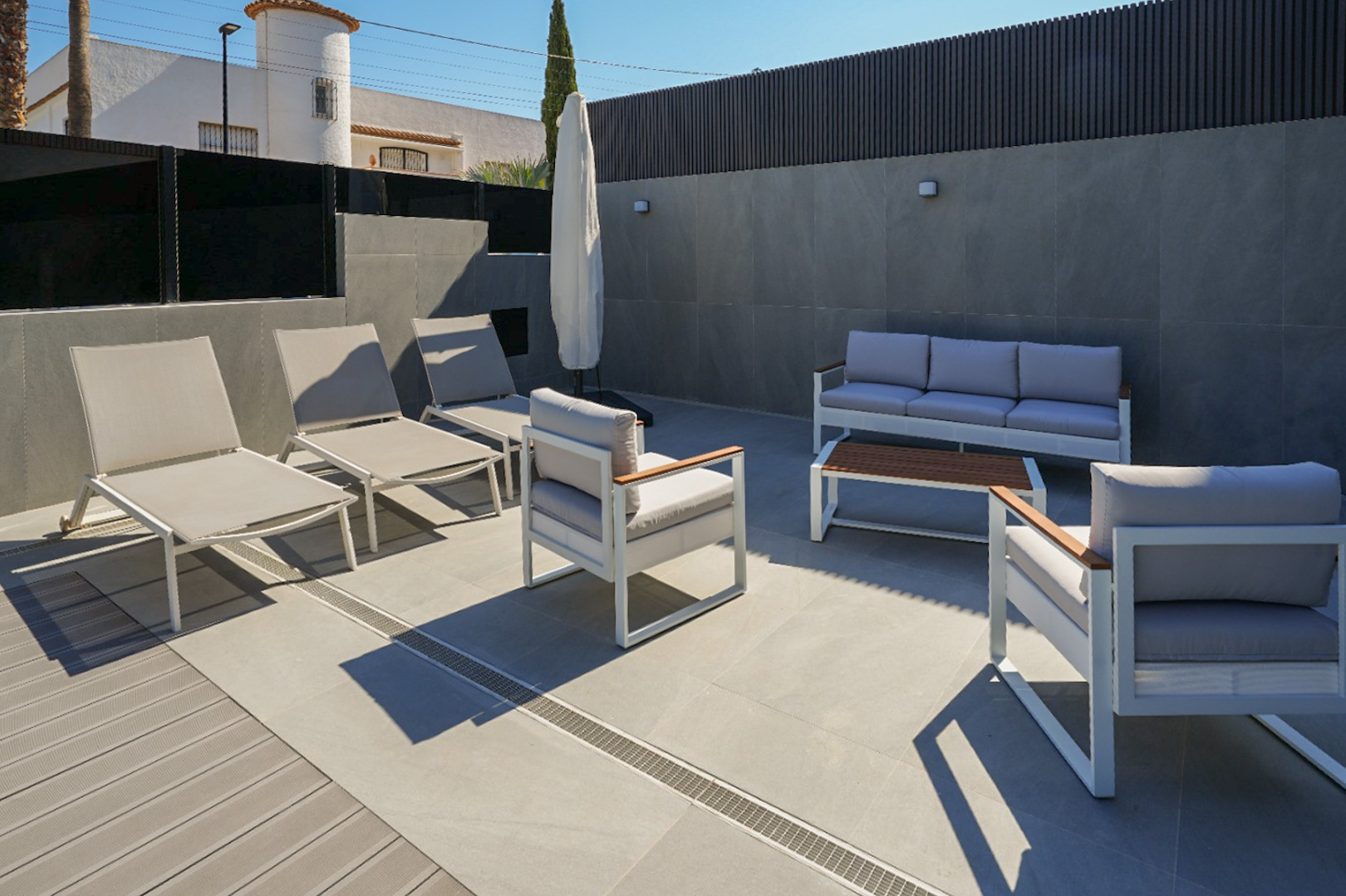 Buitenterras met modern wit-grijs lounge meubilair, gecombineerde porseleinen tegels en composiet vlonder. Ligstoelen en een zithoek zijn zichtbaar.