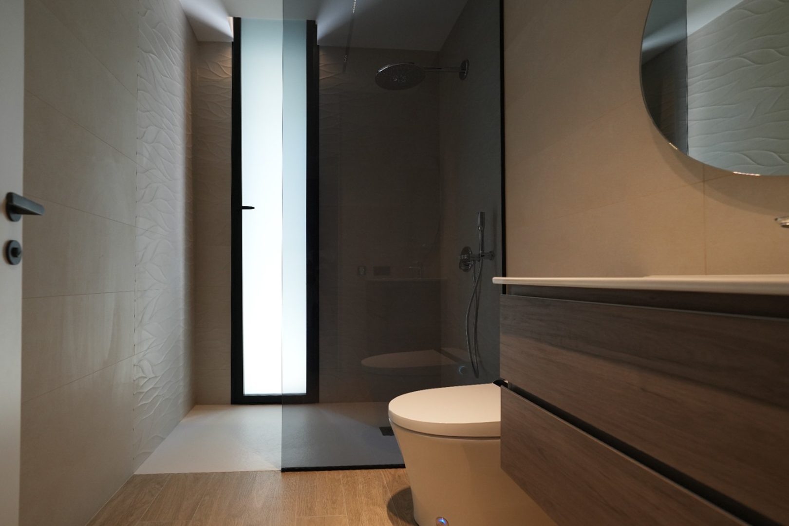 Moderne badkamer met houten badmeubel, ronde spiegel en inloopdouche. Voorzien van getextureerde wandtegels en een matglasraam.