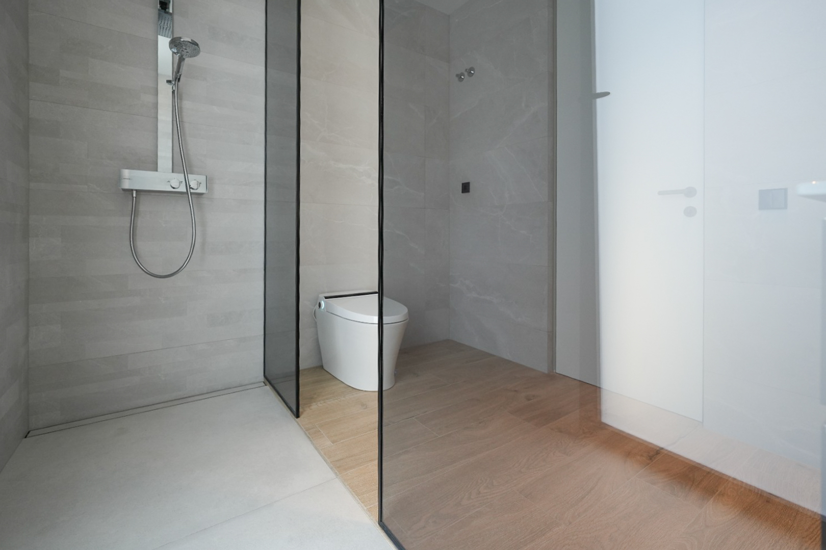 Moderne badkamer met inloopdouche, lichtgrijze tegels en chromen thermostaatkraan. Een glazen wand scheidt de douche van het smart toilet met houtnerf tegels op de vloer.
