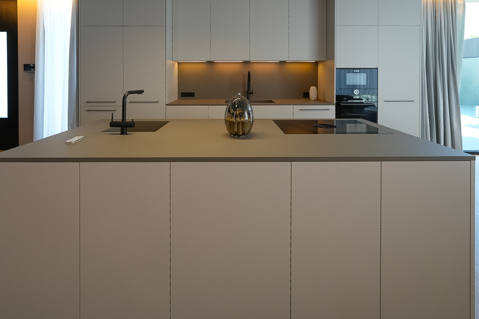 Moderne designkeuken met kookeiland, geïntegreerde spoelbak, inductiekookplaat en neutrale kasten.