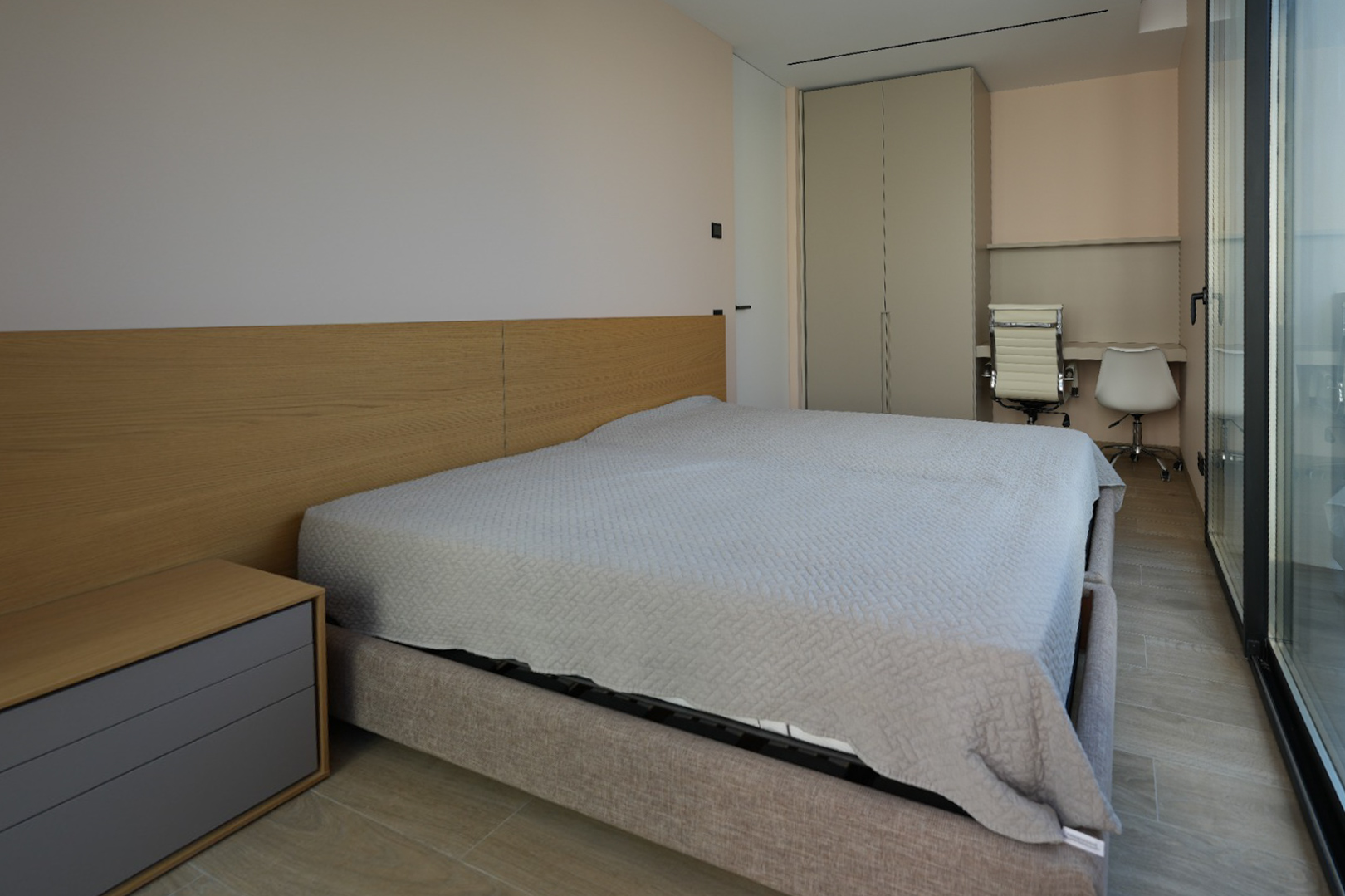 Moderne slaapkamer met lichtgrijs gestoffeerd bed, houten hoofdbord en geïntegreerd nachtkastje. Voorzien van inbouwkast, dubbele bureauhoek en grote glazen deuren.
