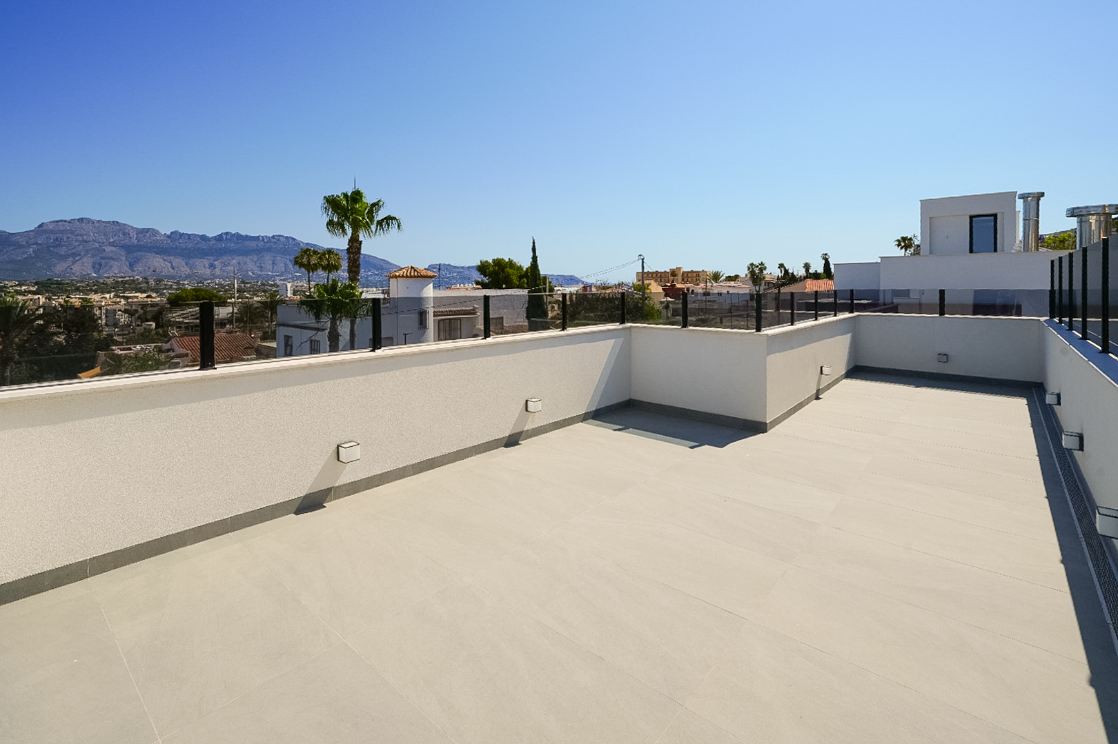 Ruim dakterras met lichte vloertegels en moderne glazen balustrade, met panoramisch uitzicht op bergen en de omliggende stad.